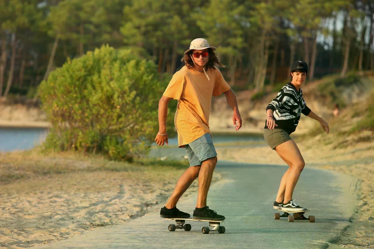 Deux skateurs sur longboard frontside, glissant sur une piste au bord d’un lac, entourés de nature.