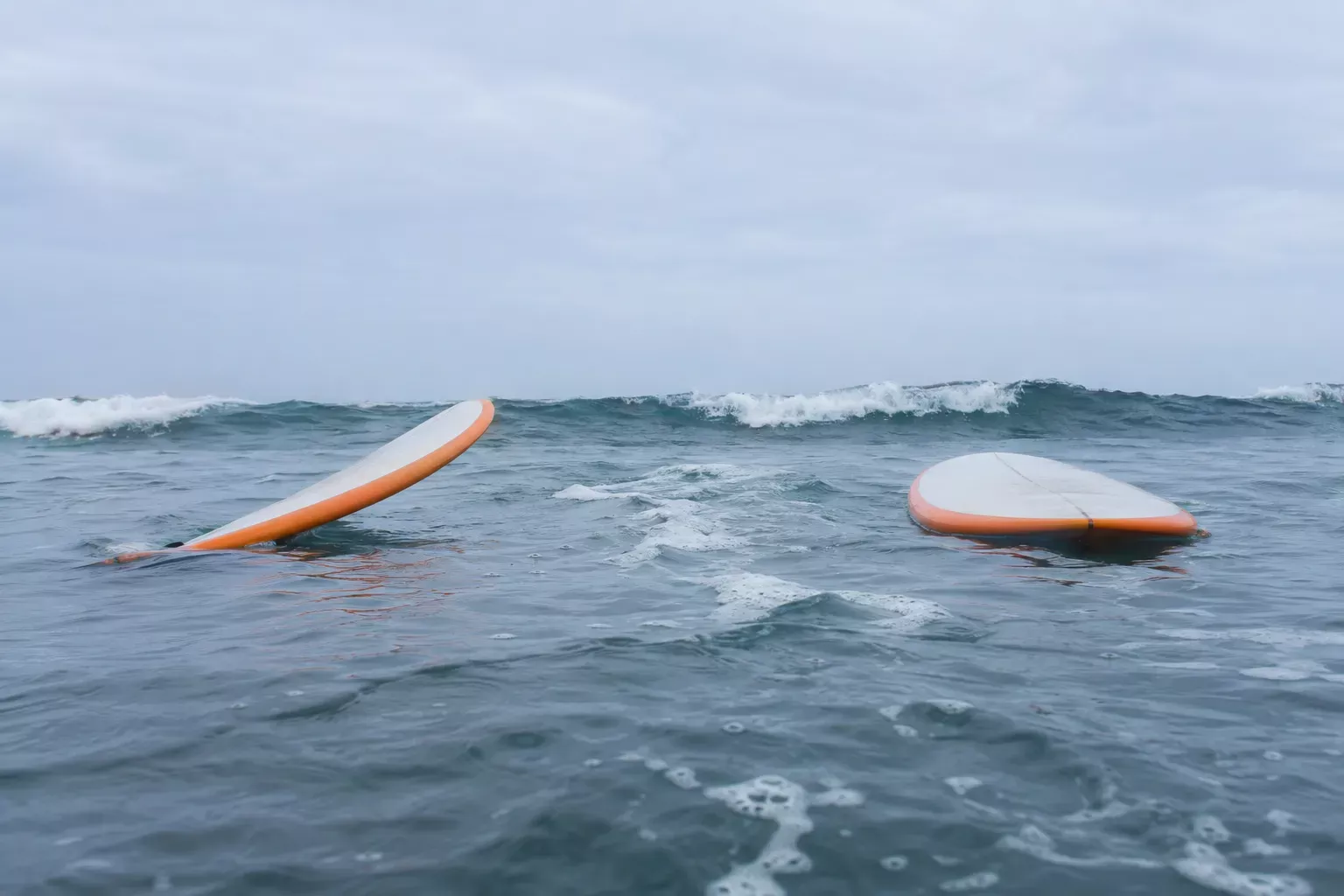 Dois surfboards alocados na água, prontos para apanhar onda, com o mar ligeiramente agitado ao fundo.