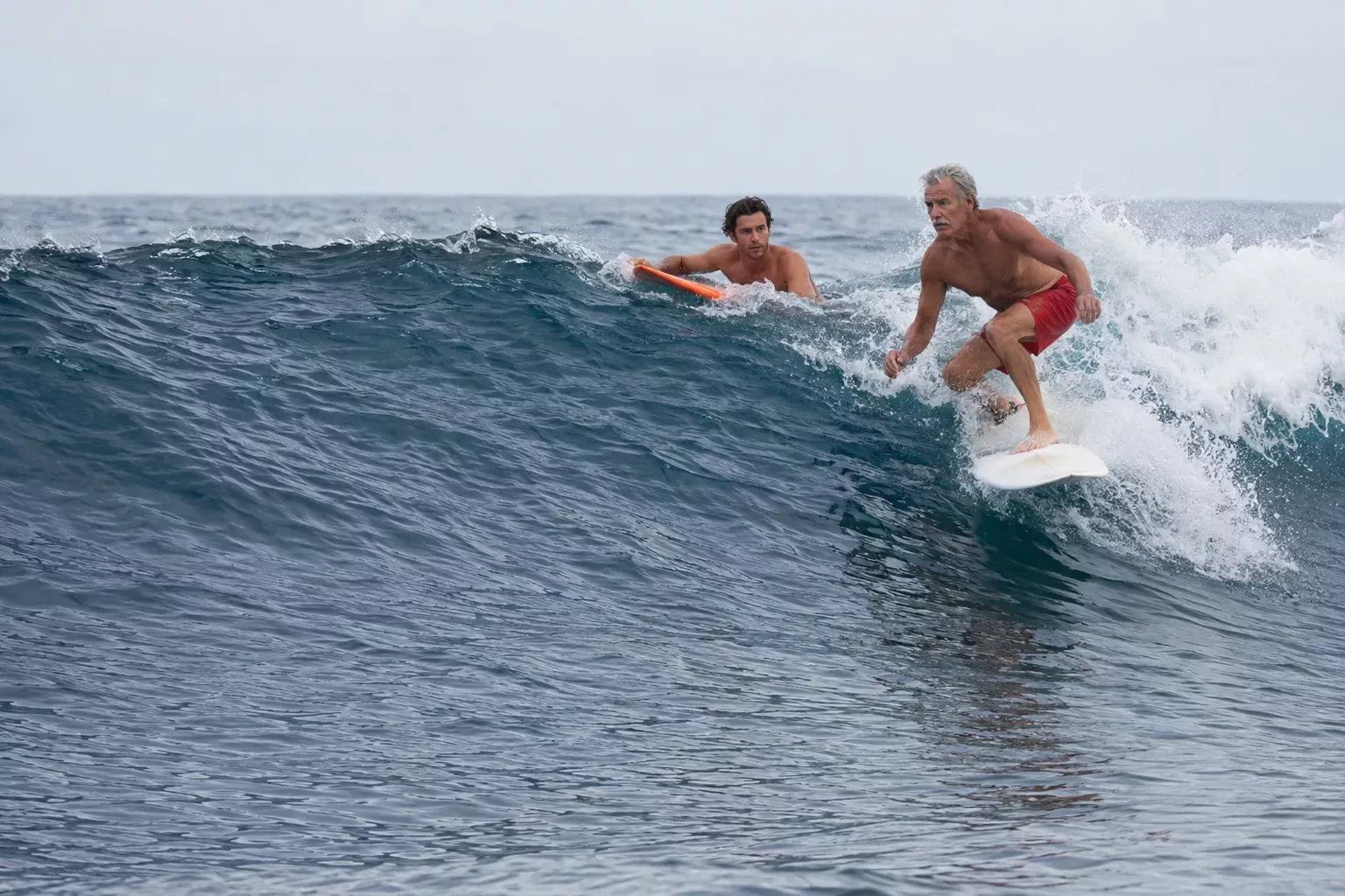 Dois surfistas numa onda, um deles em pé na prancha a deslizar na água.
