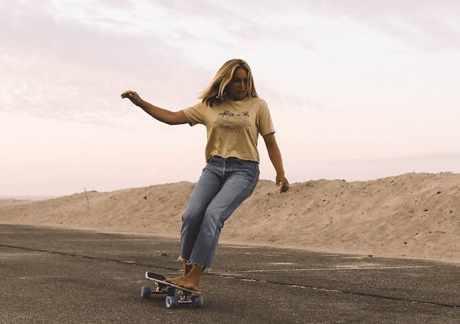 Donna che skateboards su strada deserta al tramonto, stile rilassato e chill.