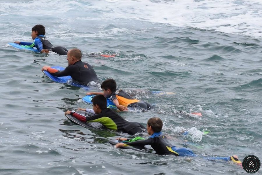 Groupes de surfers adultes et enfants apprenants, sur des planches de bodyboard et de surf, à la surface des vagues.