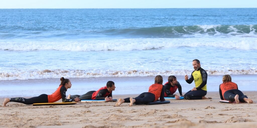 Grupo de personas en una playa entrenando surf con colchonetas, escuchando a un instructor.