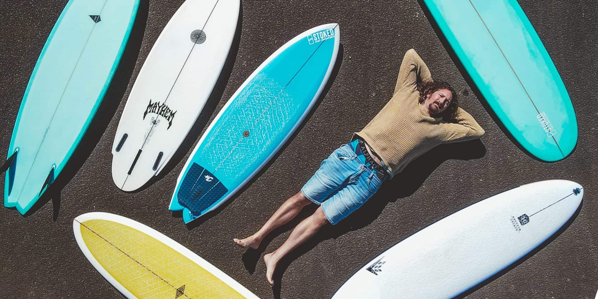 Homme allongé sur le sable entouré de planches de surf colorées, prêt pour la session.