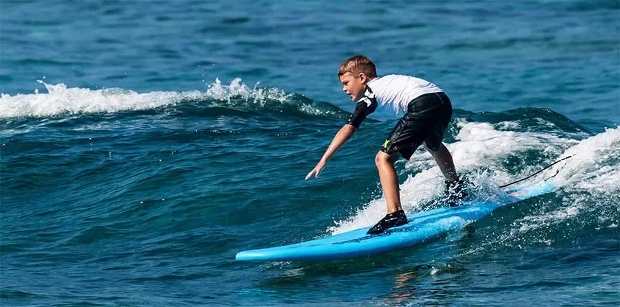 Joven montando una tabla de surf sobre una ola blue en el mar.