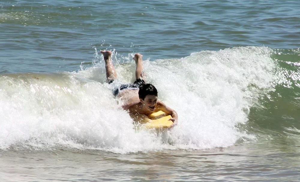Junger Mann surft auf einer Welle mit einem gelben Bodyboard am Strand.