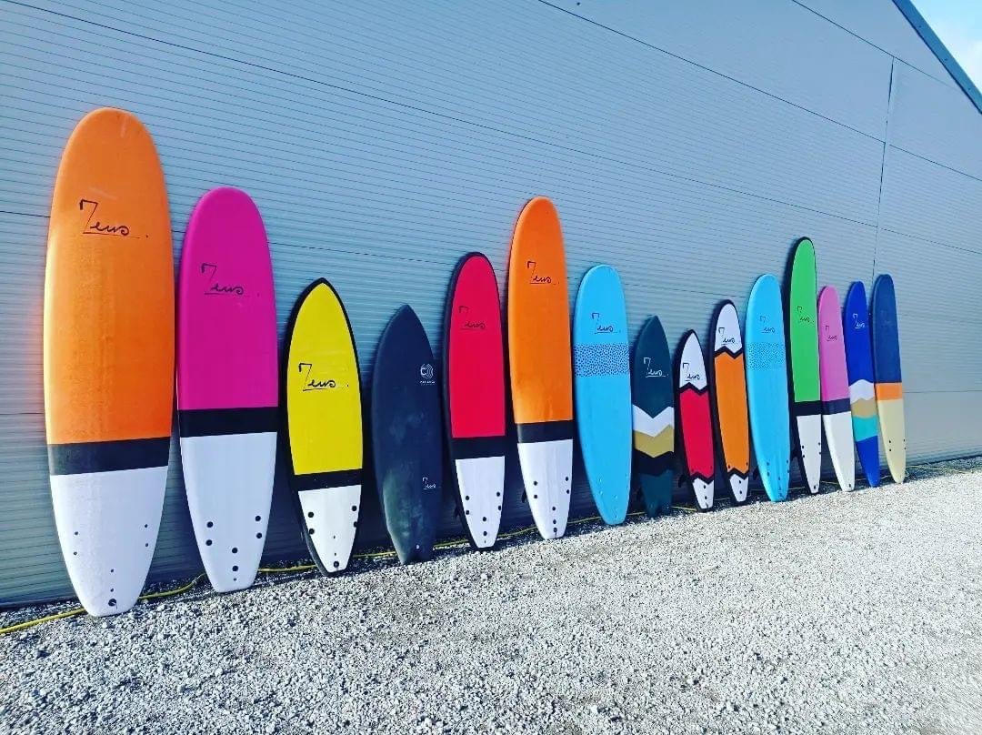 Longue rangée de planches de surf colorées appuyées contre un mur gris à l'extérieur.