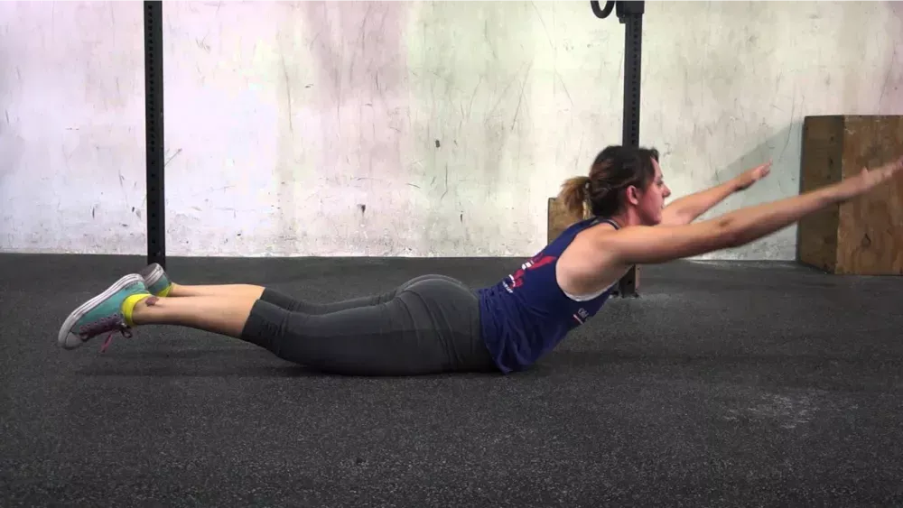 Mujer haciendo ejercicio de plancha extendida en el suelo, cuerpo paralelo al piso y brazos adelantados.