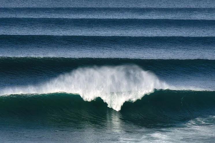 Onda perfetta che rompe, cresta alta e spruzzi d’acqua bianca sull’oceano.