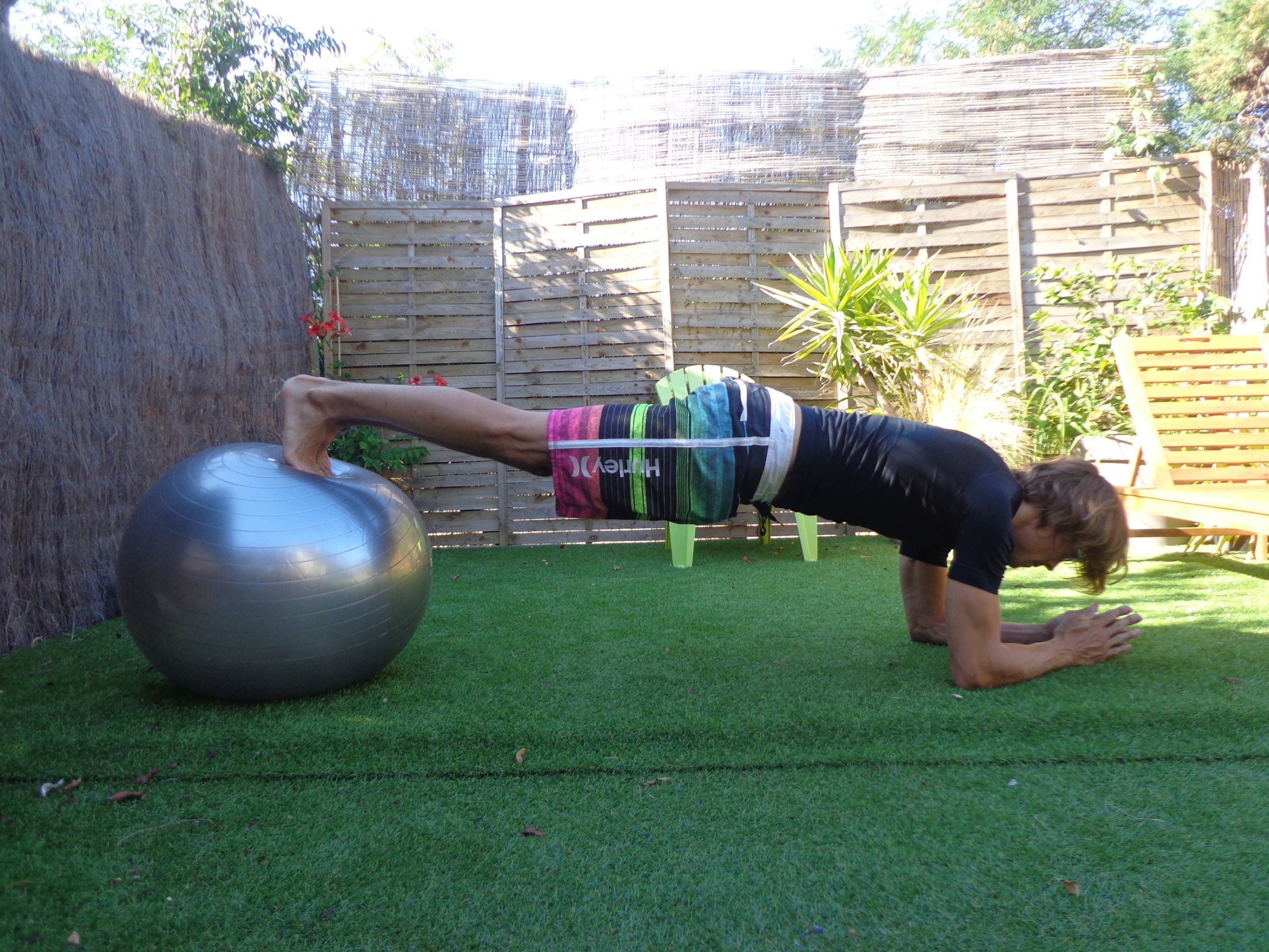 Person macht eine Bauch-Übung mit Fitness-Ball im Garten, Kopf unten, Füße auf dem Ball. | Ideal: "Fitness-Übung im Garten: