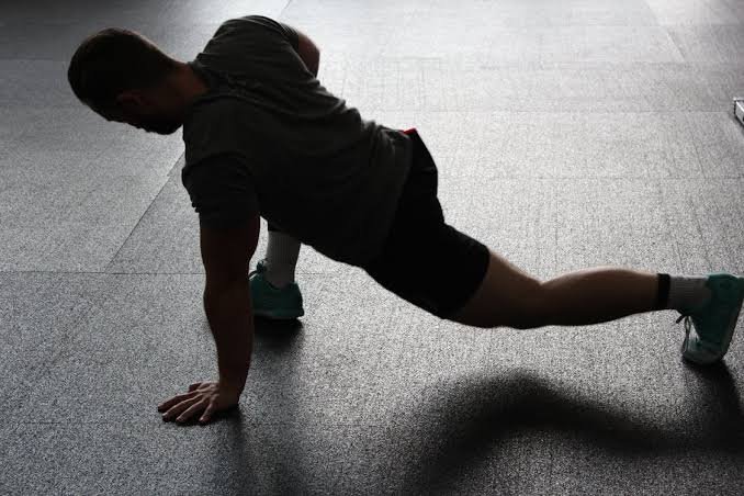 Person macht eine seitliche Ausgleichs- oder Liegestütz-Position auf einer Sporthalle; trainiert Core und Schulterstabilität.