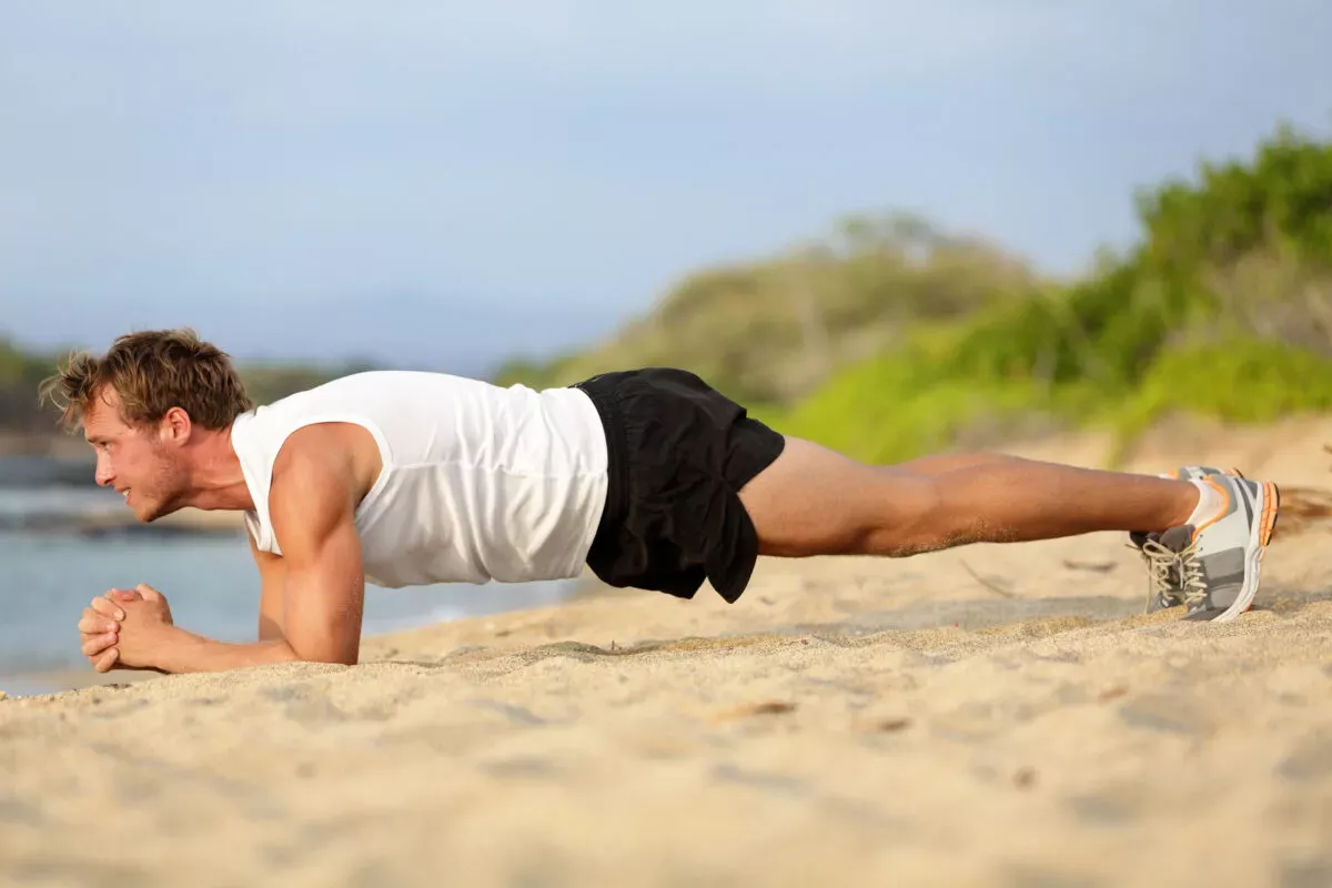 Persona haciendo una plancha en la playa, con cuerpo alineado y barbil desde el suelo. Keyword integrada: entrenamiento en la playa.