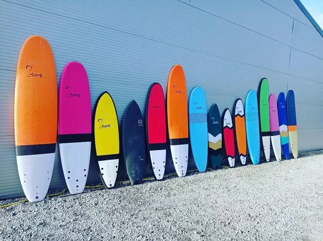 Pranchas de surf coloridas alinhadas em fila against uma parede metálica, exibindo tons vibrantes e diferentes modelos.