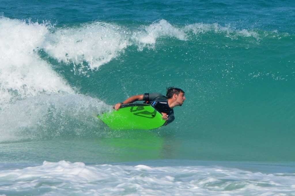 Ragazzo in corsa su una tavola da surf verde neon in una onda oceánica.