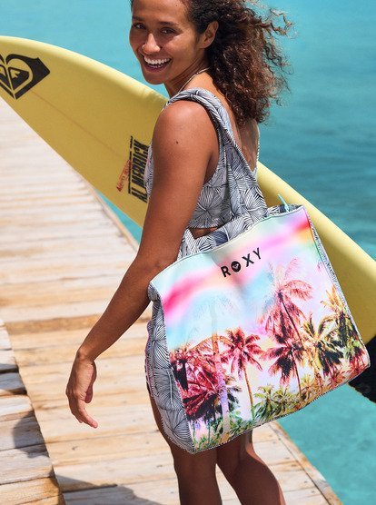 Sac fourre-tout coloré à palmier, porté sur l’épaule d’une surfeuse près de la plage avec planche jaune.
