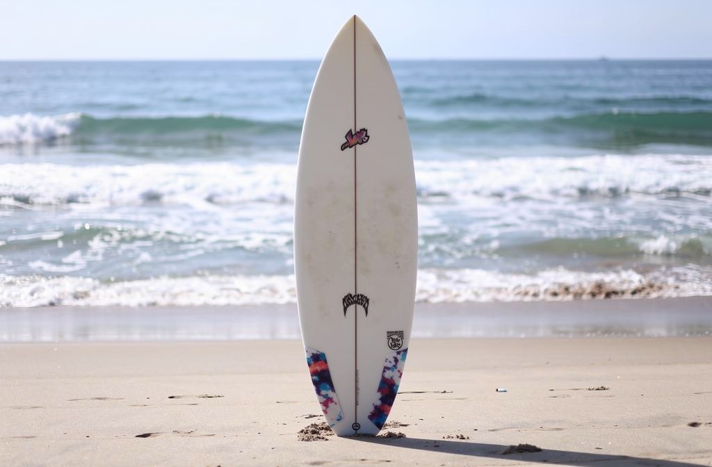 Surfbrett steht senkrecht im Sand am Strand, Meer und sanfte Wellen im Hintergrund : bereit zum Surfen. Ab welcher wellenhöhe ist surfen geeignet.
