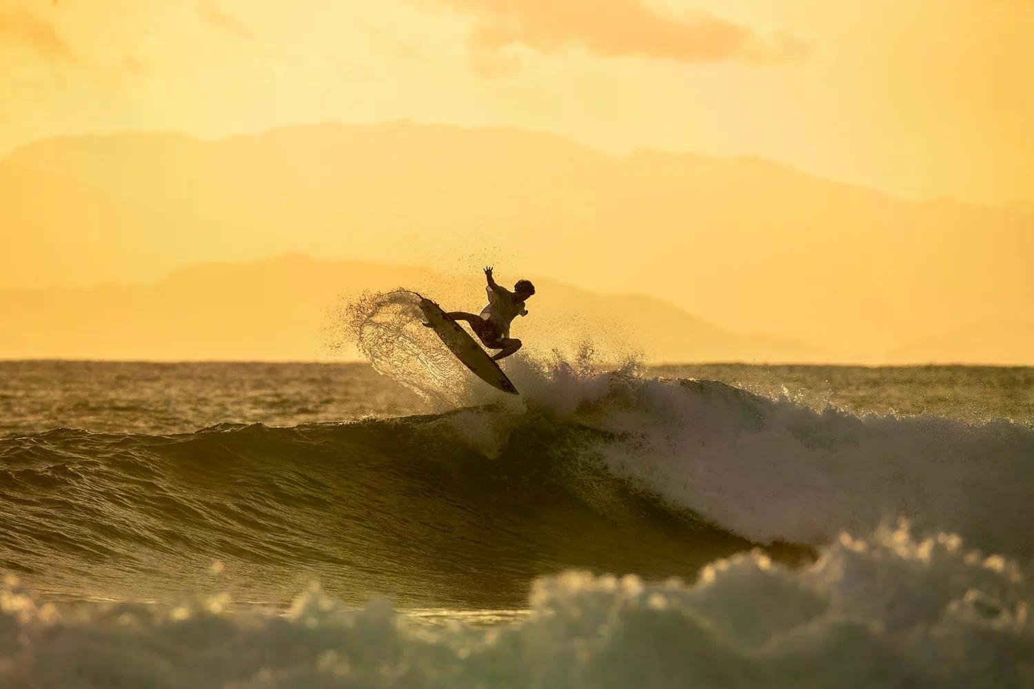 Surfer beim Sprung über eine Welle im goldenen Sonnenuntergang, Surf-Action am Meer.