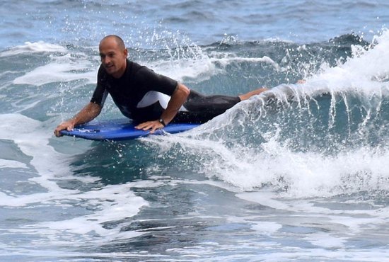 Surfer in a black wetsuit riding a blue shortboard on a small wave, spray splashing around.