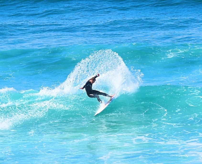 Surfer auf grün-blauer Welle, hinten spritzt Wasser beim Kickturn, dynamic Surfaction.