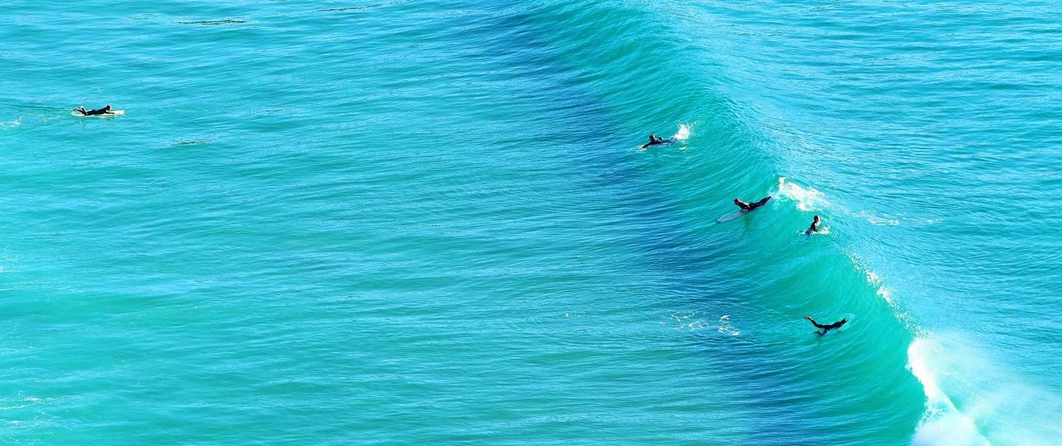 Surfer in klarer Meeresbrandung, Wellen reiten an der Küste entlang, türkises Wasser.