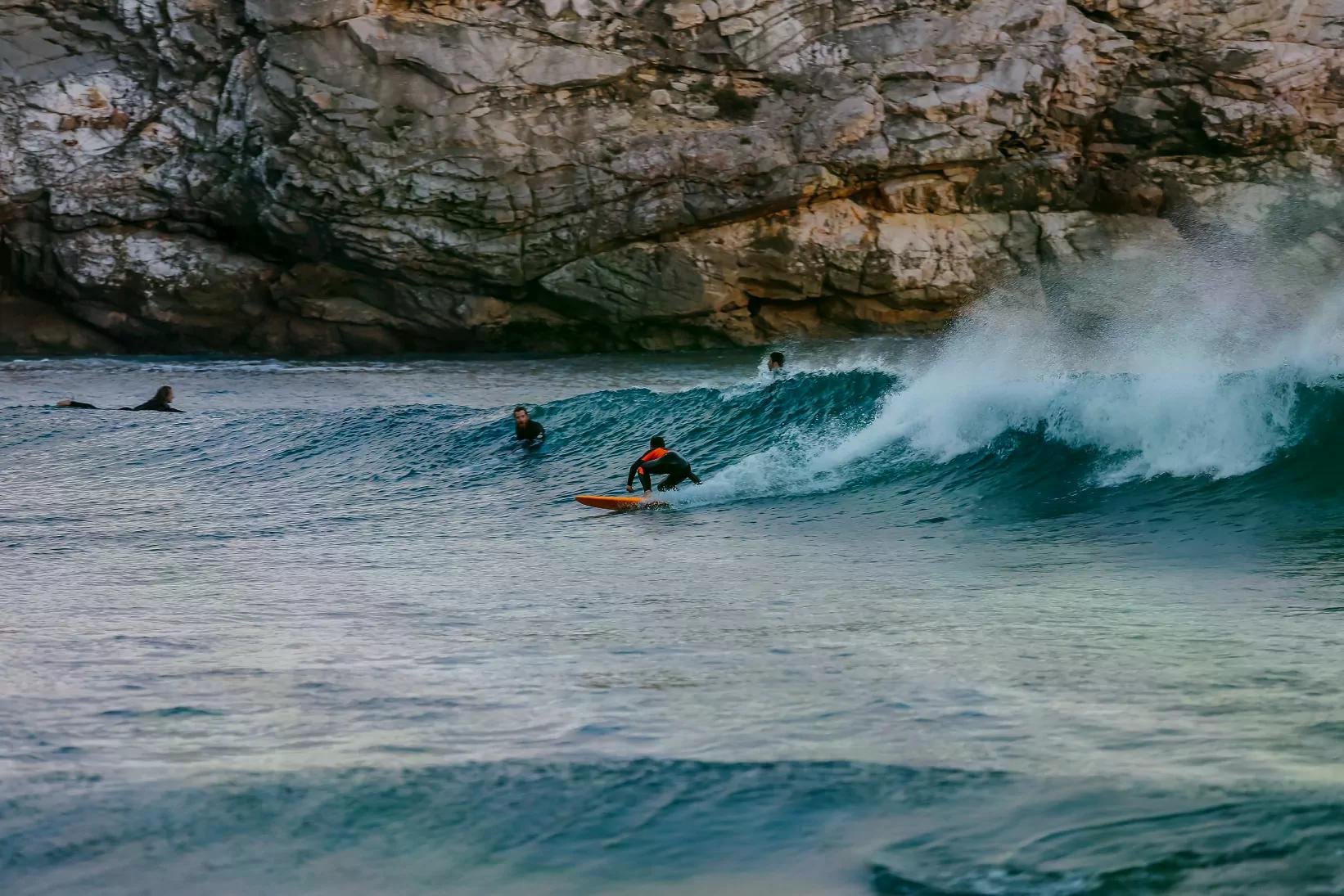 Surfer auf einem kleinen Shortboard reitet eine grüne Welle nahe Felsenküste.