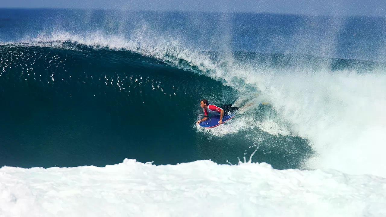 Surfer riding inside a big turquoise barrel on a breaking wave, sunlit spray.