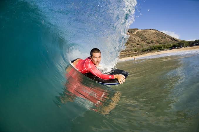 Surfer riding inside a turquoise barrel, wearing a red wetsuit on a shortboard.
