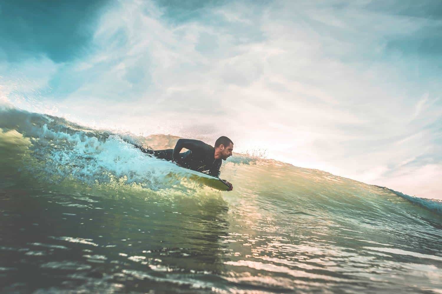 Surfer riding a translucent green-blue wave, cropping water spray as he glides forward.