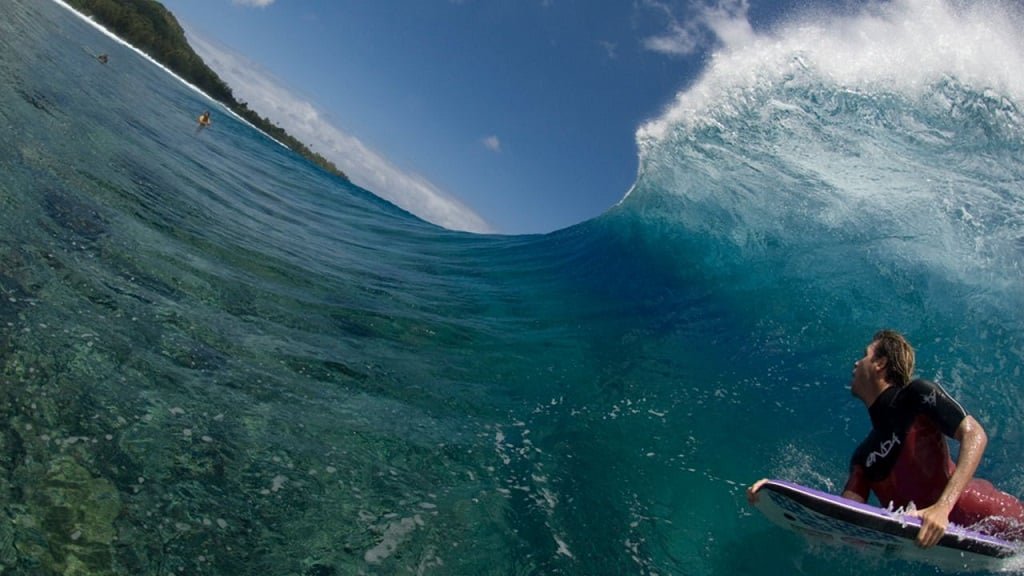 Surfer in Türkisblauem Meer reitet eine große Brecherwelle, Blickwinkel von der Wasseroberfläche aufgenommen.