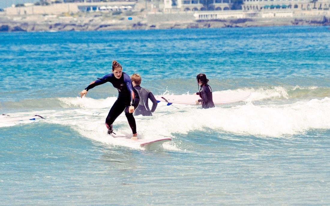 Surferin auf dem Stand-Up-Board vor der Küste, zwei weitere Surfer im Hintergrund beim Lernen im flachen Wasser.