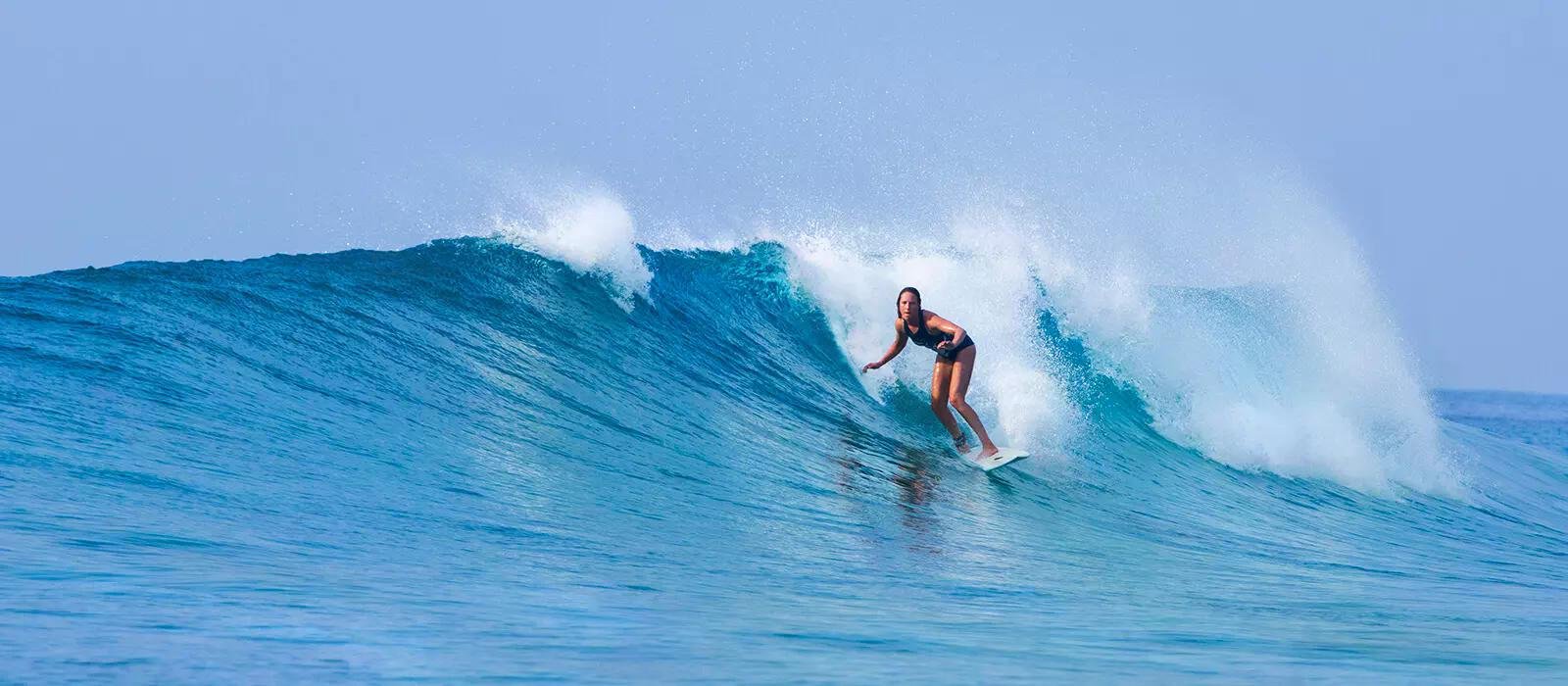 Surfeuse sur une grande vague bleue en glisse, posture équilibrée sur la planche dans l’océan.