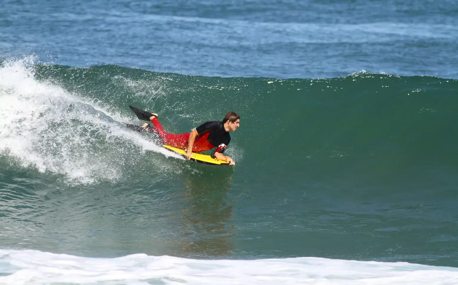 Surfista a apanhar uma onda verde com prancha amarela, em posição de curva no esbarro da crista.