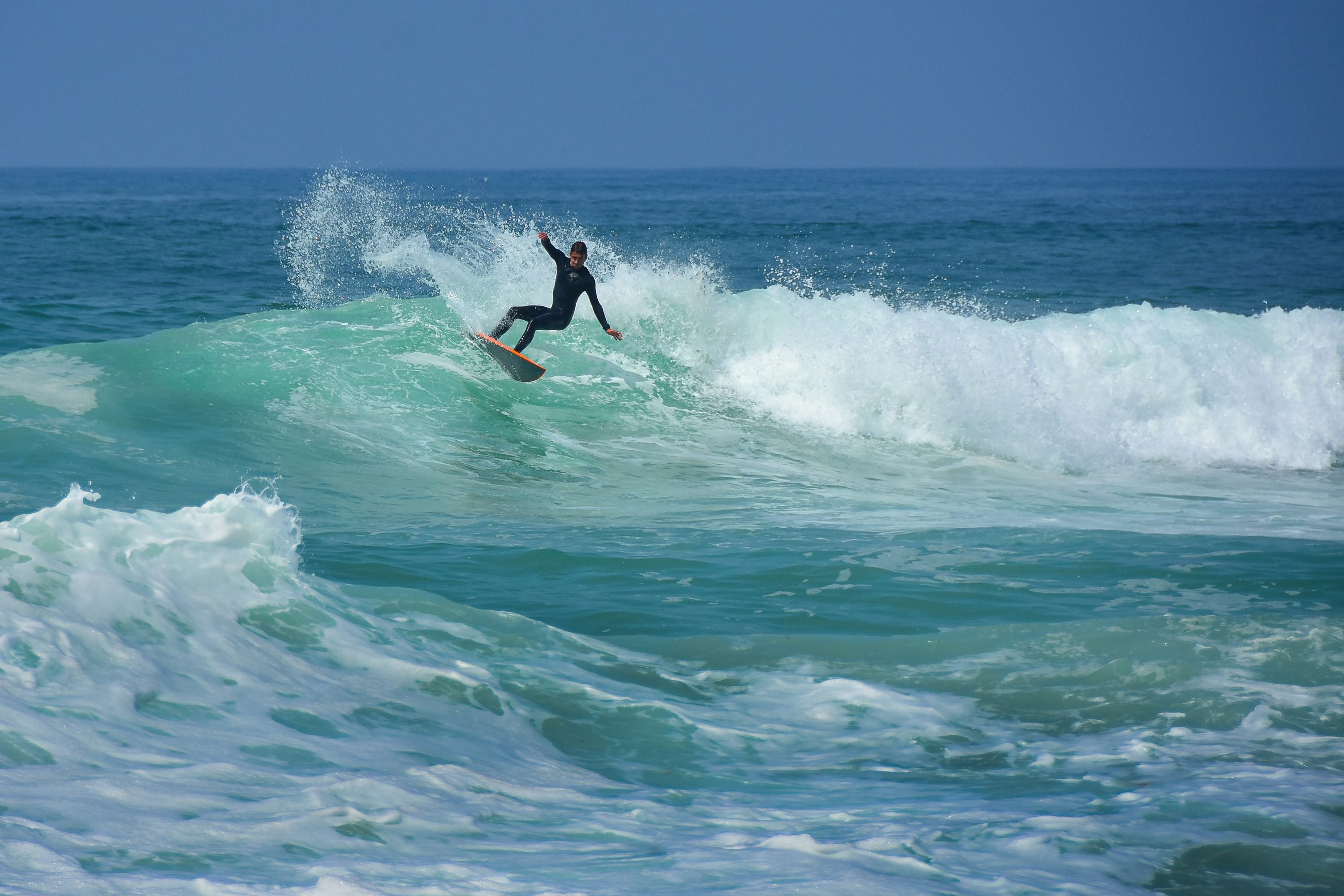 Surfista a dominar uma onda, em posição de take-off num mar azul com espuma branca.