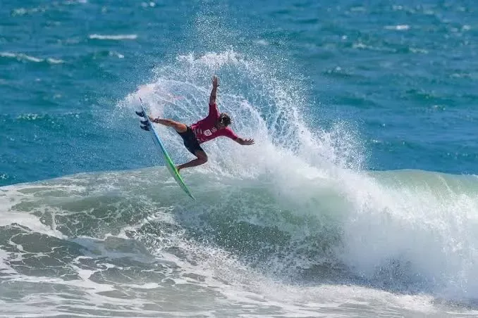Surfista a fazear manobra acrobática numa onda, spray de água ao redor.