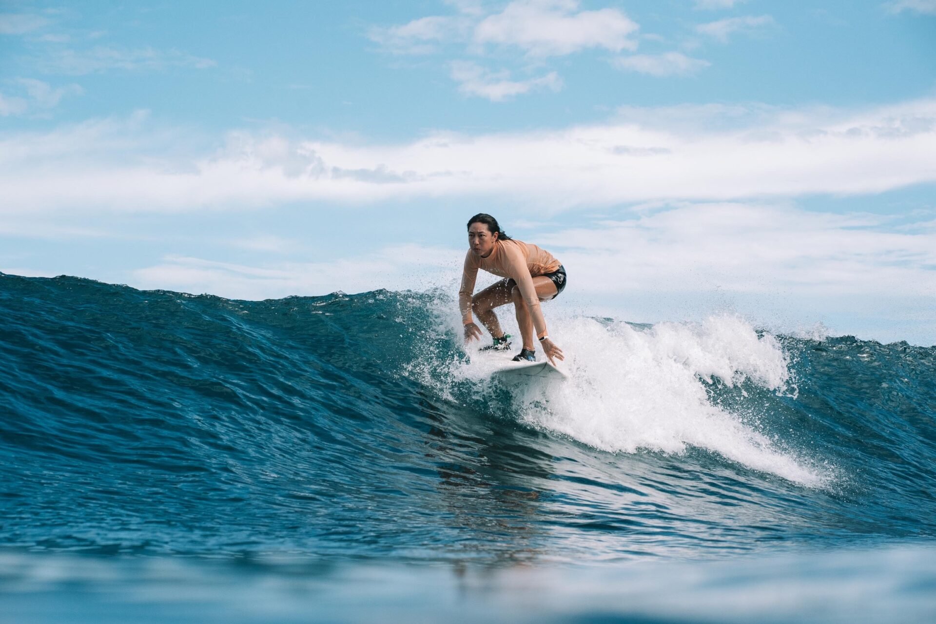 Surfista femminile in ginocchio sull’onda, pronta a scivolare lungo la cresta.