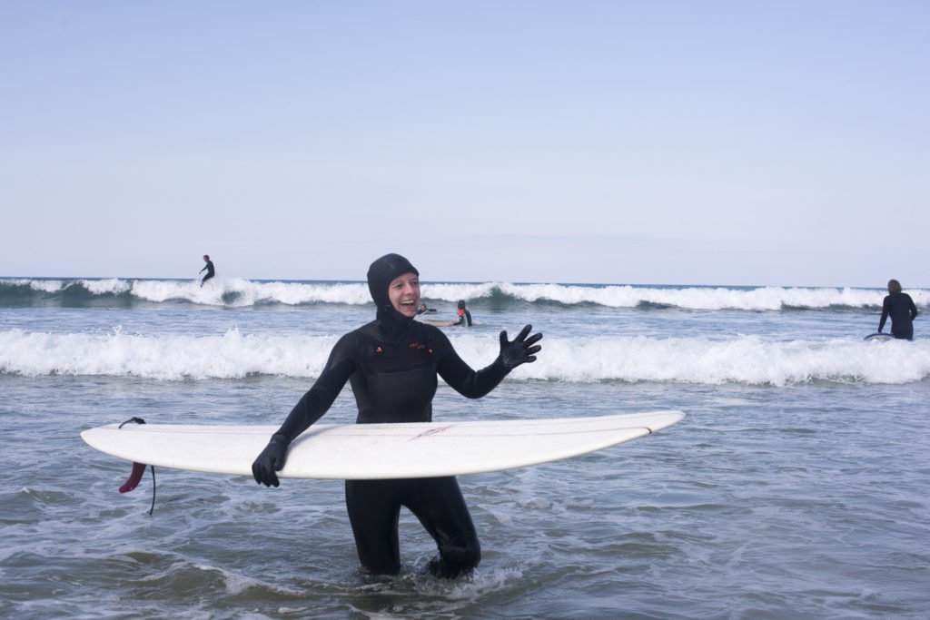 Surfista in mare aperto con muta integrale, hold surfboard bianca in mano.