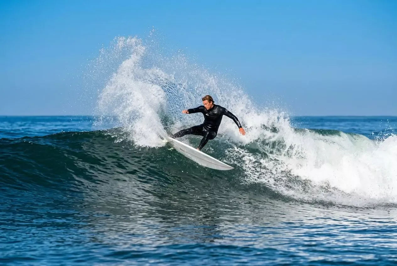 Surfista montando una ola con derrame de agua, practicando maniobra en el oleaje azul. Perfecto para aprender a surfear como principiante.