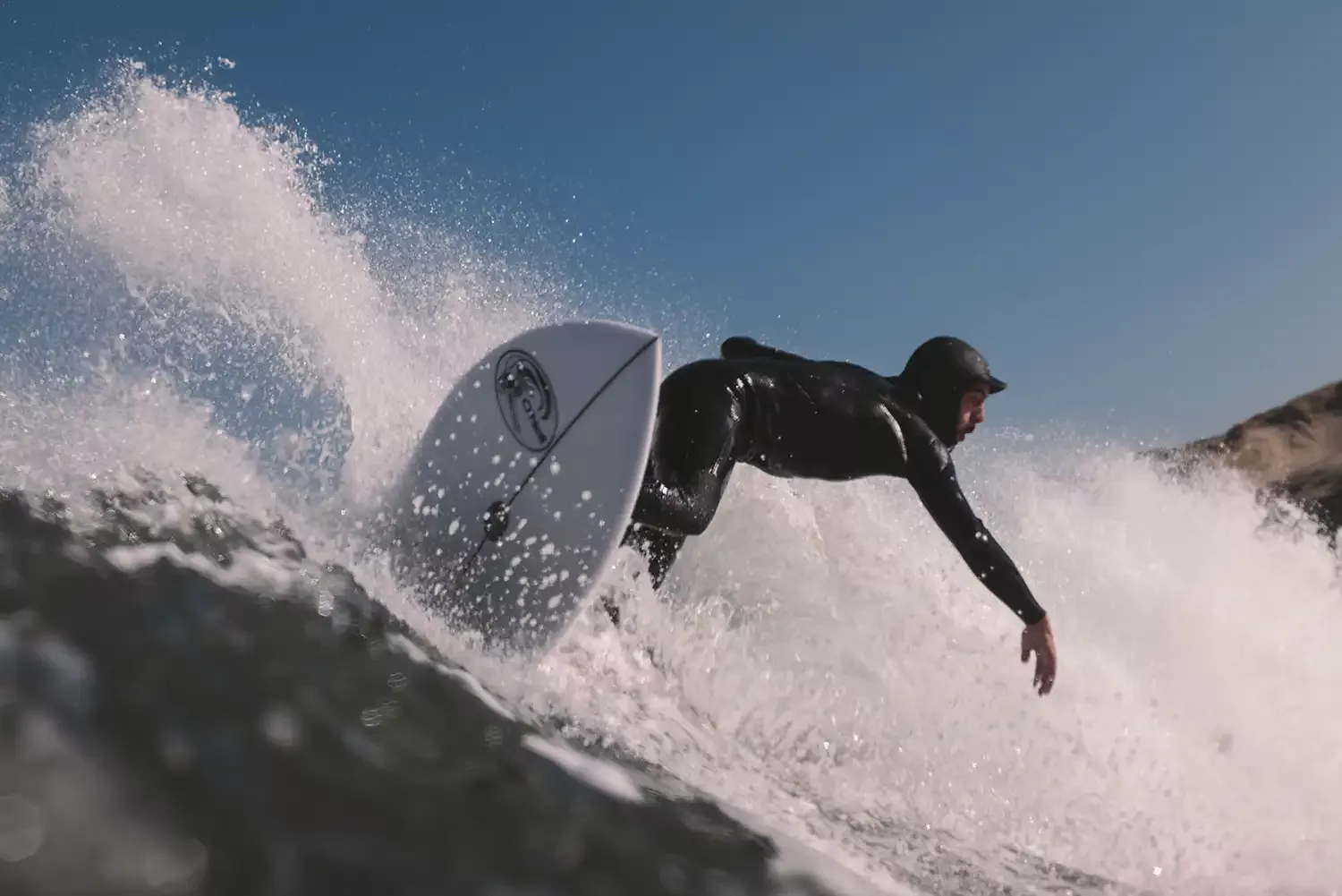 Surfista montando una ola con la tabla de surf inclinada hacia adelante, en acción dentro del agua.