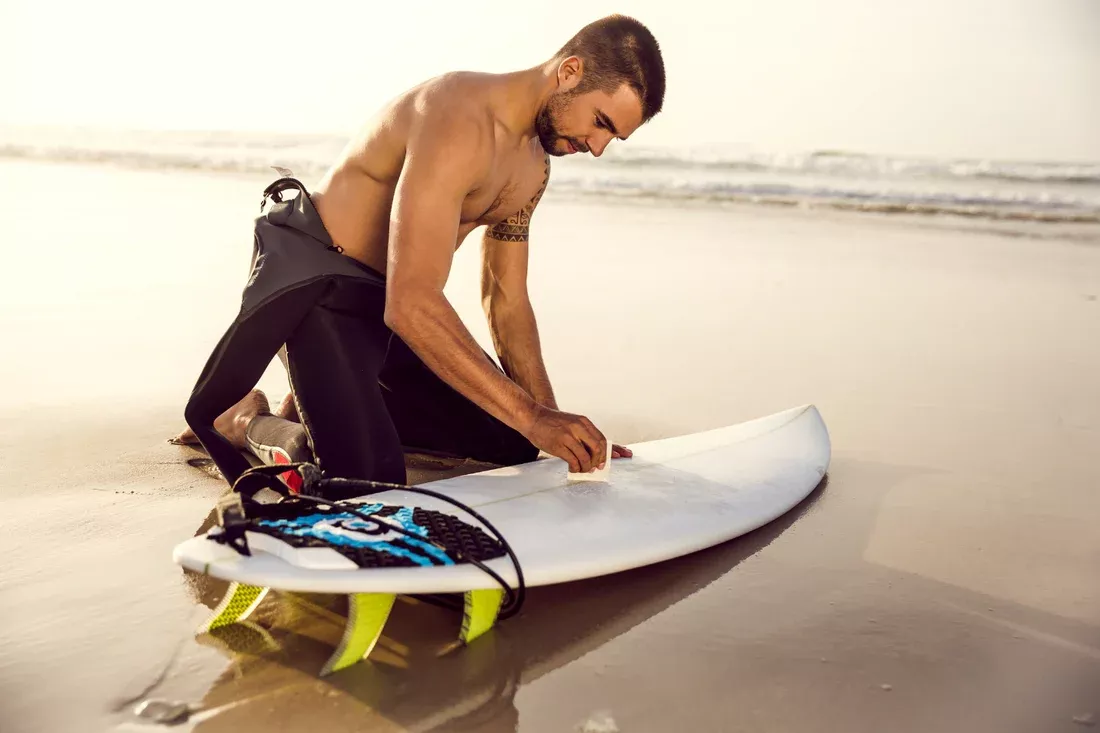 Surfista en la playa ajustando una tabla de surf en condiciones soleadas.