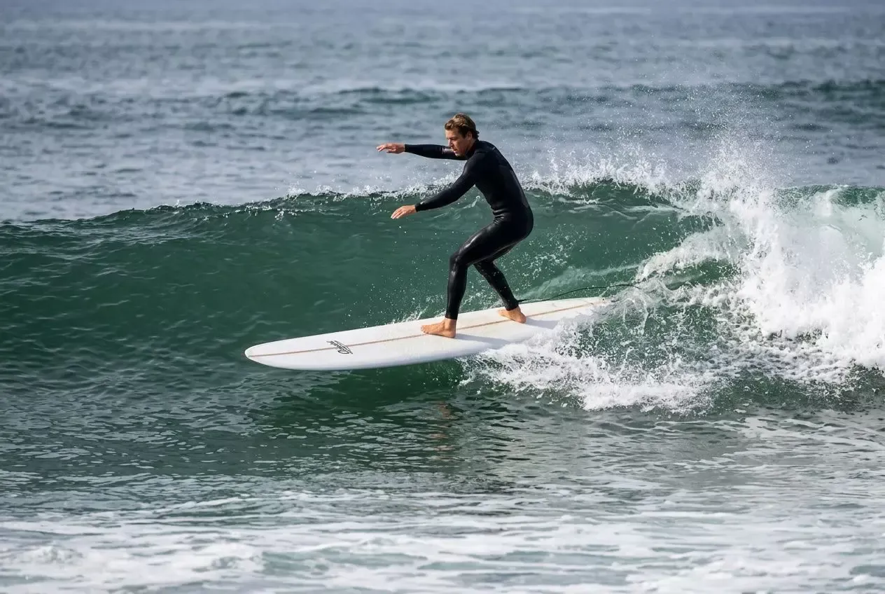 Surfista em prancha de surf longboard para iniciantes, deslizando em onda suave com traje completo.