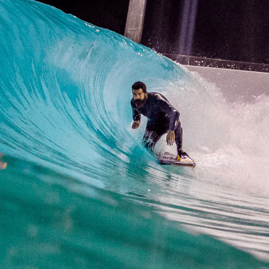 Surfista surfeando una ola azul dentro de un tubo, con mirada concentrada y tabla bajo los pies.
