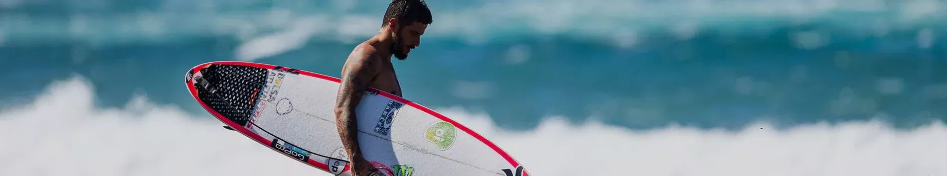 Surfista con tabla de surf blanca y roja caminando sobre las olas en playa.
