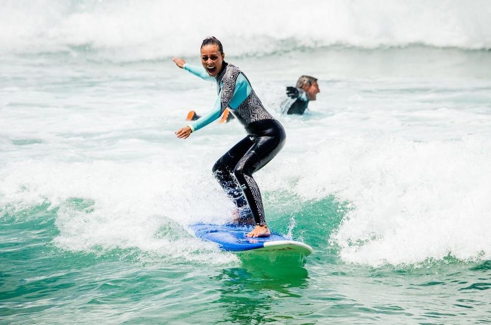 Surfista in tavola da surf sulle onde, sorriso e equilibrio, con compagno in secondo piano. Alt text per surf.
