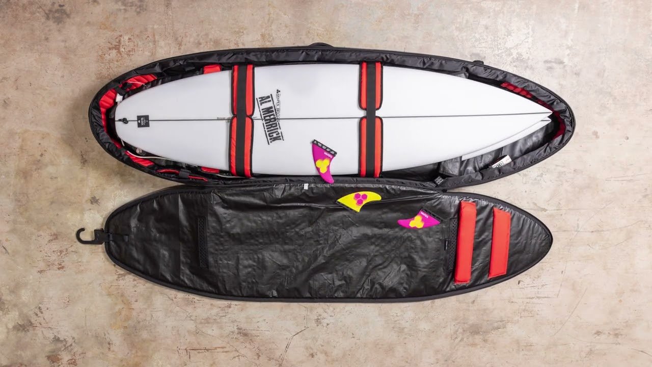 Tabla de surf y funda rígida acolchada, listo para viaje, con toques rojos y calcomanías en blanco y negro. Se aprecia una tabla dentro de su sleeve protector.