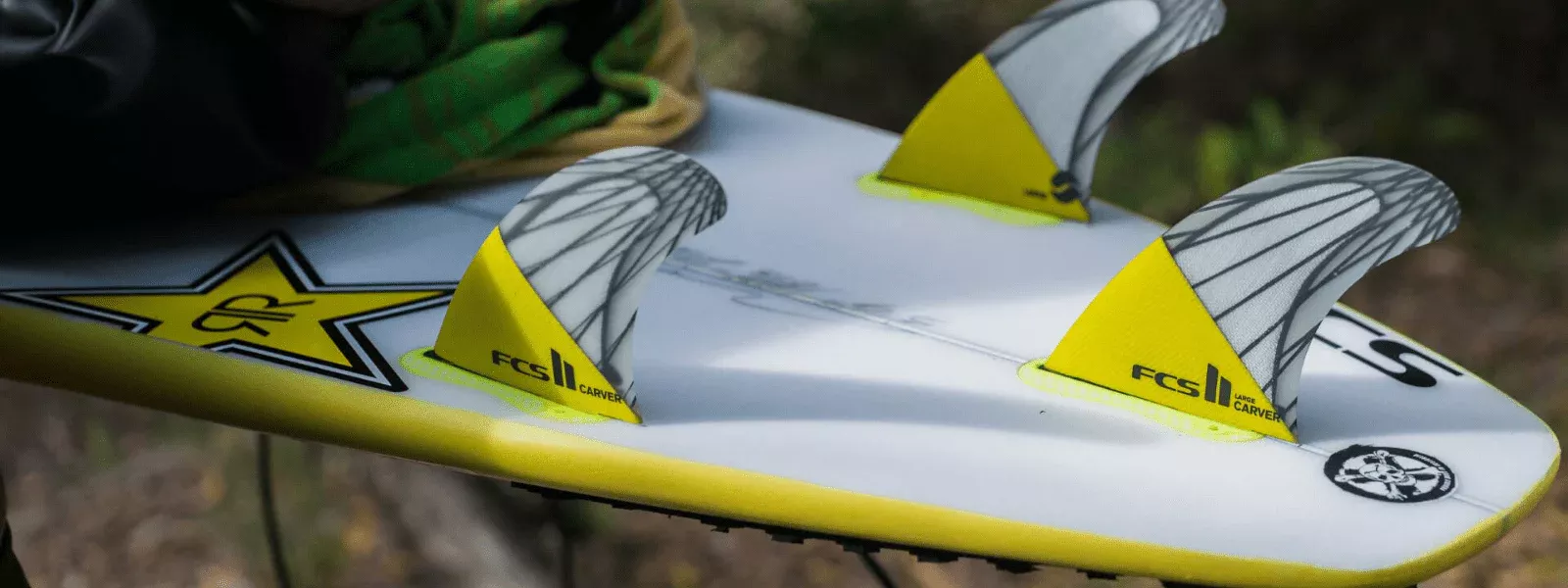 Tablas de surf con aletas amarillas de fijación, sobre una tabla blanca y borde amarillo.
